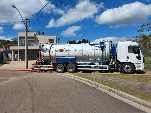Lateral de caminhão com tanque e mangueiras junto a acesso pavimentado.