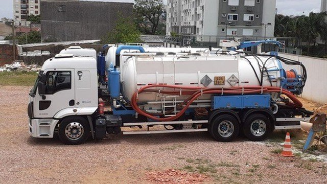 Caminhão de sucção de perfil em pátio de terra.