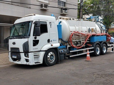 Caminhão e utilitário com marca Previni em rua junto a edifício.