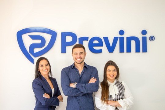 Três pessoas diante da marca Previni em parede clara.