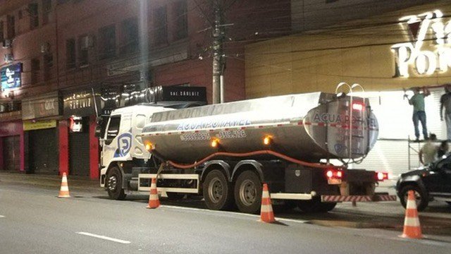 Caminhão com mangueira em via urbana durante a noite.