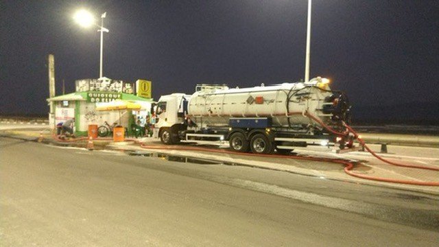Atendimento noturno em posto de combustível, com caminhão e mangueira.